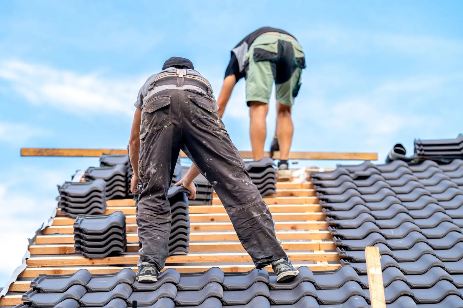 Two roofers setting new tiles on a roof