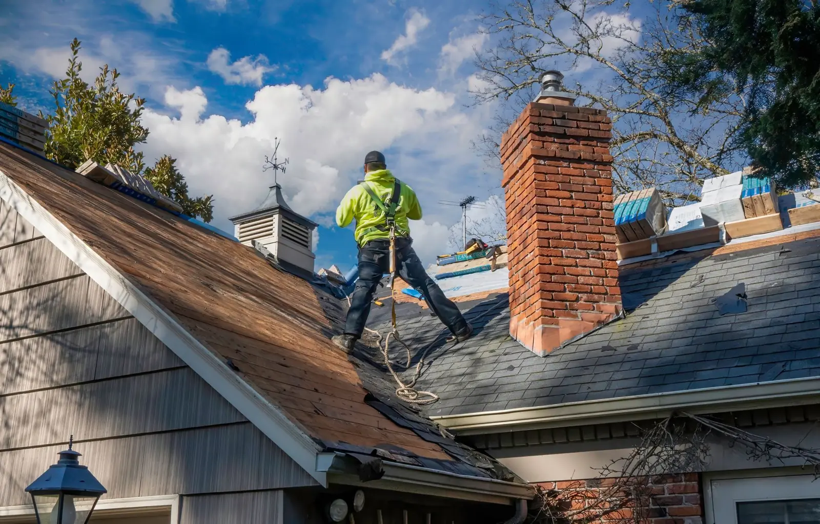 Roofer repairing storm damage on a shingle roof beside a chimney